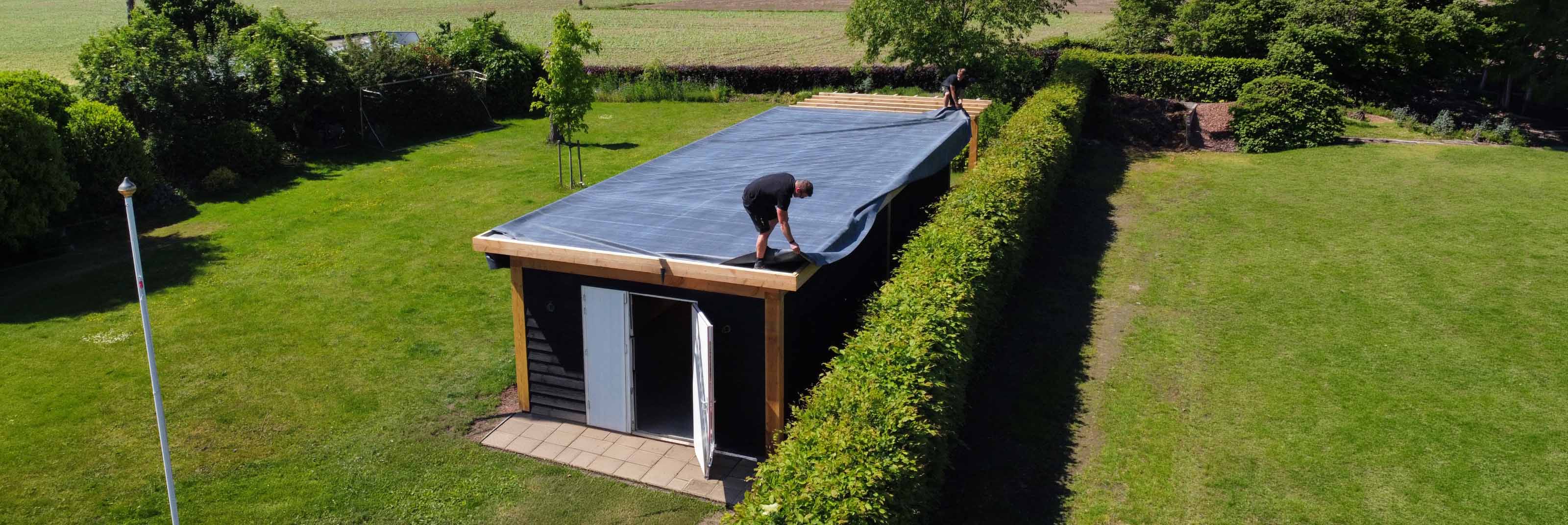 Twee dakdekkers leggen EPDM-folie op het platte dak van een tuinhuis