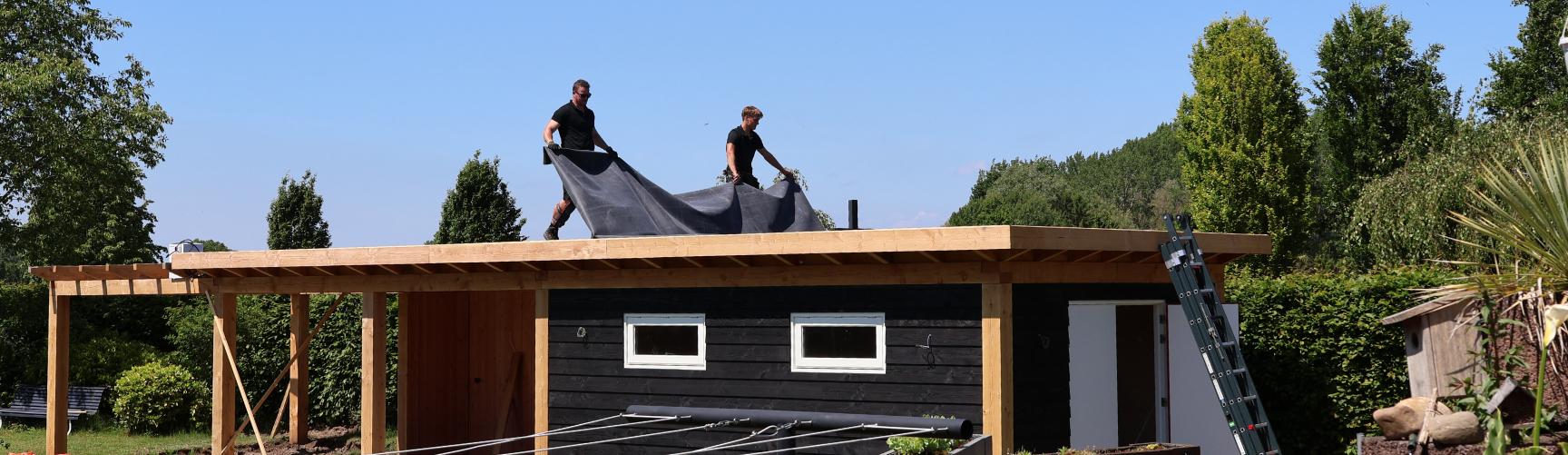 Twee dakdekkers leggen EPDM-folie op het dak van een tuinhuis